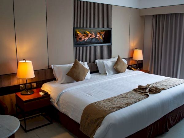 A modern hotel room with a neatly made bed, warm lamps, and a built-in fireplace feature.