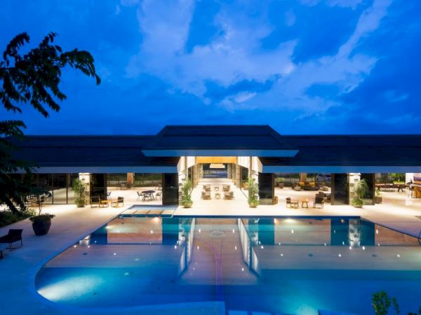 An outdoor resort pool at dusk with sunlit loungers beneath a modern building and palms.