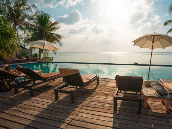 A sunny beachfront resort deck with lounge chairs, umbrellas, and a calm ocean view at sunset.