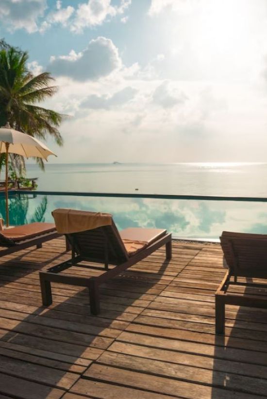 A sunny beach resort deck with lounge chairs, umbrellas, and calm ocean views under a bright sky.