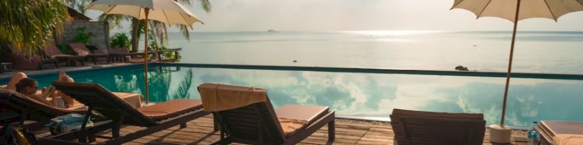 A seaside resort deck with lounge chairs and umbrellas overlooking calm ocean at sunset.