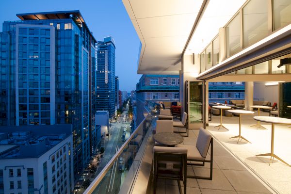 Modern office balcony with lounge seating overlooking downtown buildings and streets at dusk.