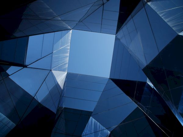 Futuristic building made of blue glass panels and geometric facets, photographed upward against the sky.