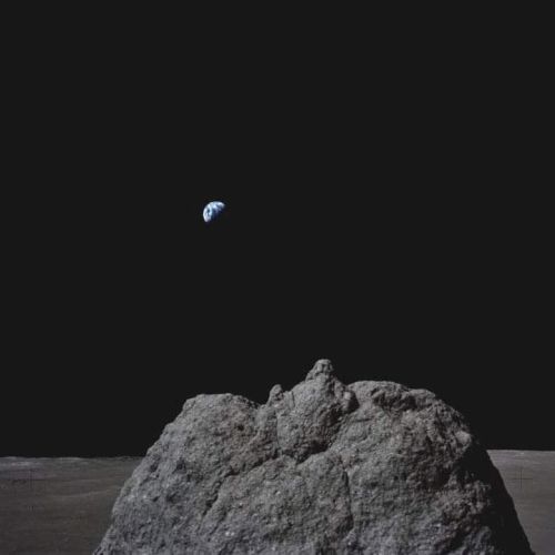 A small blue planet-like orb floats above a rough gray rock in a dark, minimal scene.