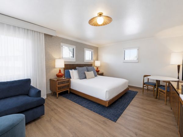 A bright, modern bedroom with a large bed, blue chairs, side tables, and a ceiling lamp.
