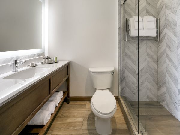 A modern bathroom with a vanity sink, white toilet, and a glass shower with folded towels.