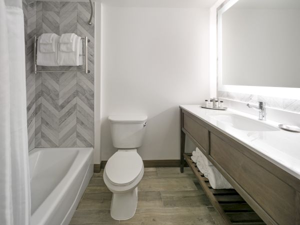 Bright modern bathroom with a tiled shower, folded towels, toilet, and a white countertop vanity.