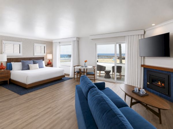 Bright coastal suite with a blue sofa, bed, wall TV, fireplace, and beach-view windows.