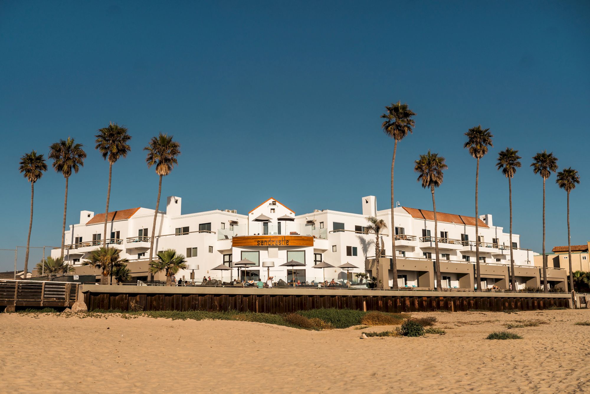 A beachfront resort building with palm trees under a clear blue sky.