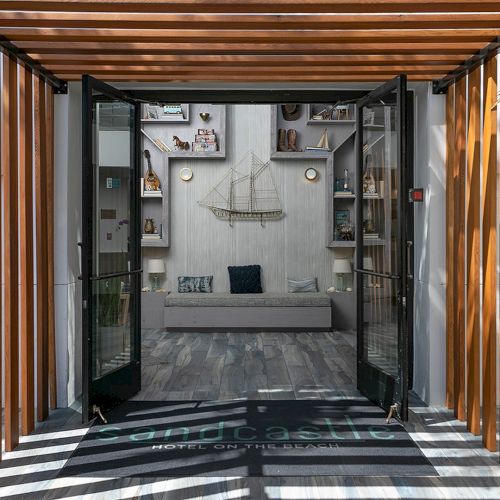 A hotel outdoor corridor with wooden slatted walls, glass doors, and a central lounge bench beneath shelves and decor.
