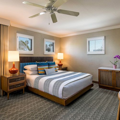 A modern hotel bedroom with a neatly made bed, bedside lamps, curtained windows, and a flat-screen TV.