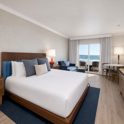 A modern seaside hotel bedroom with a large bed, bedside lamps, ocean-view window, and a TV in a cozy suite.
