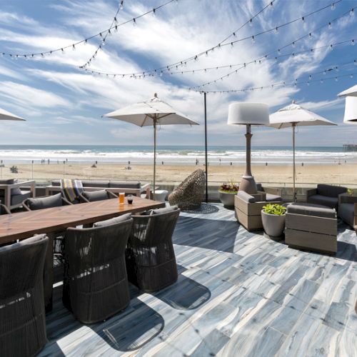 Rooftop patio with outdoor lounge chairs, tables, umbrellas, string lights, and a view of the beach and ocean.