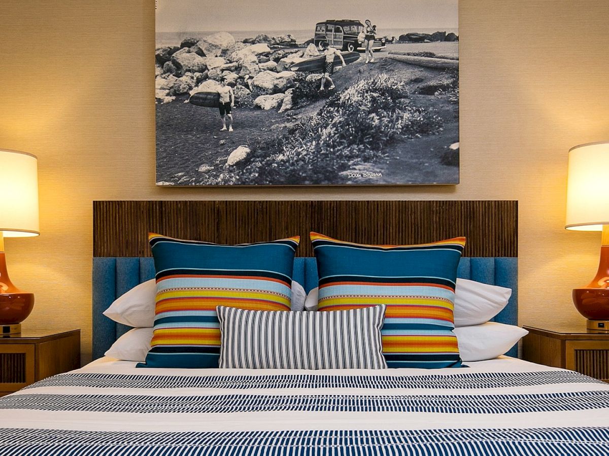 A neatly made bed with colorful striped pillows, two matching bedside lamps, and a black-and-white wall art piece above the headboard.