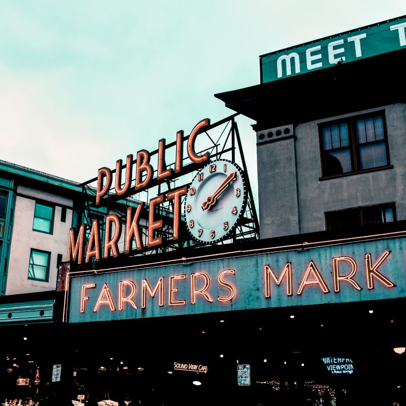 A building facade with a neon clock sign reading &ldquo;Meet the Dublin Farmers Market.&rdquo;