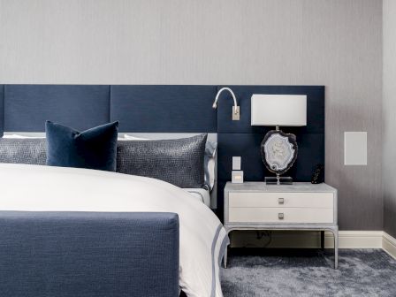 A modern hotel bedroom: blue bed with pillows, bedside table holding a lamp, geode decor, remote, and clock.