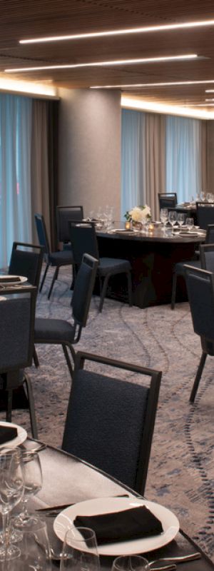 A set banquet hall with round tables, place settings, glassware, floral centerpieces, and chairs under warm ceiling lights.