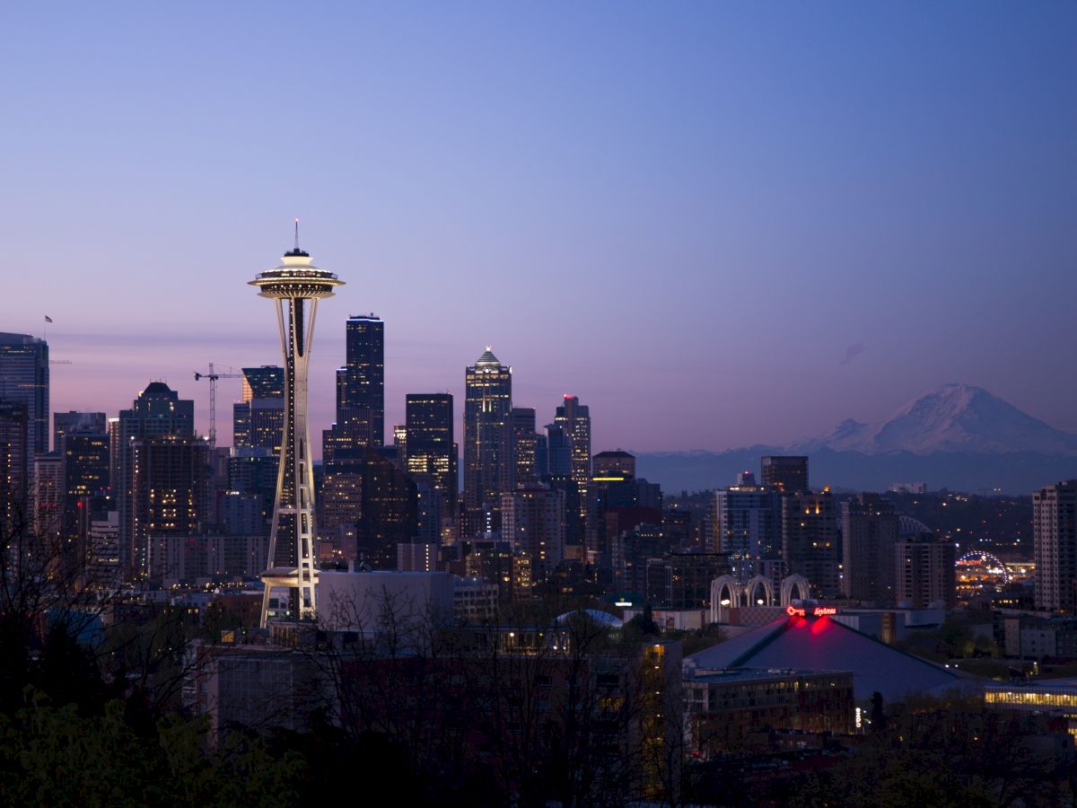 Seattle&rsquo;s skyline at dusk, featuring the Space Needle rising above city buildings and distant mountain haze.