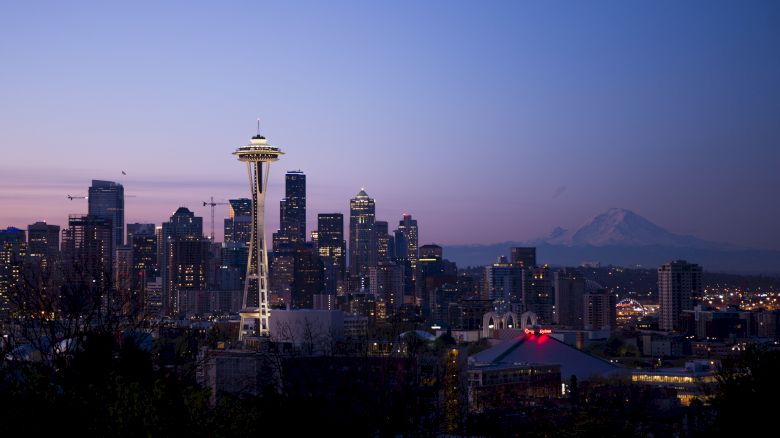 Seattle&rsquo;s skyline at dusk, featuring the Space Needle rising above city buildings and distant mountain haze.