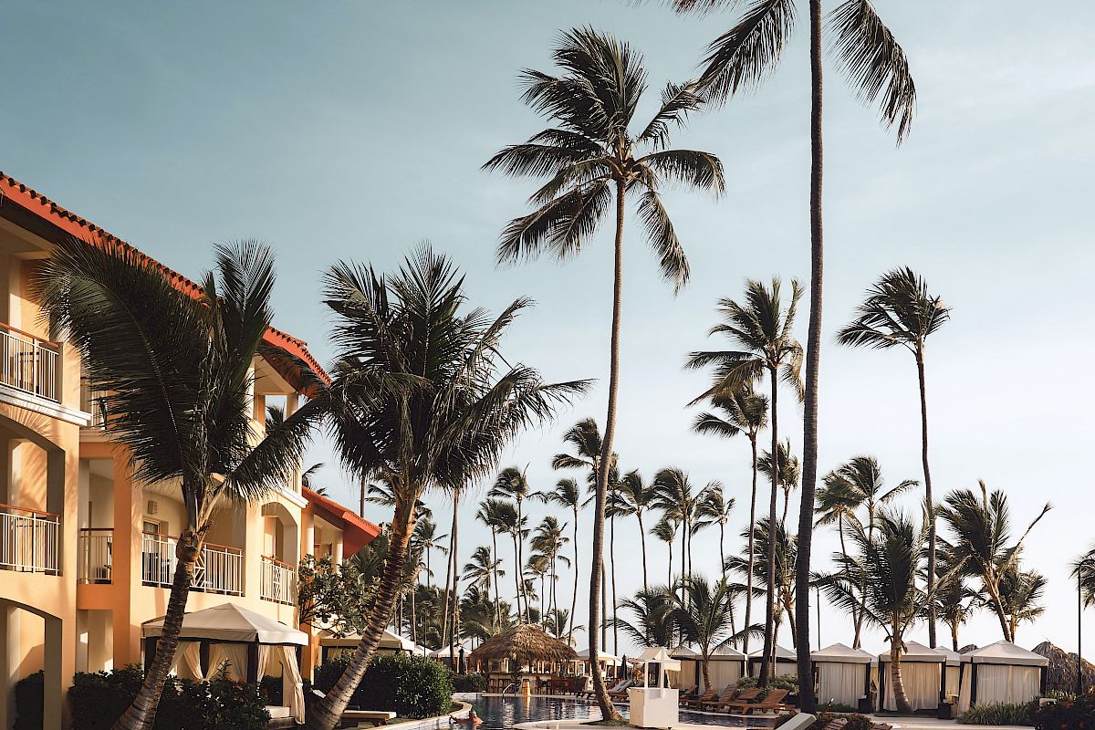 A tropical resort pool with palm trees, lounge chairs, and white cabanas under a bright blue sky, for a relaxing vacation vibe.
